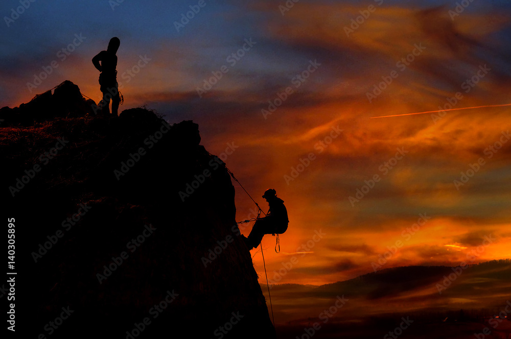 Climber waiting his partner on the summit. Beautiful sunset in the background