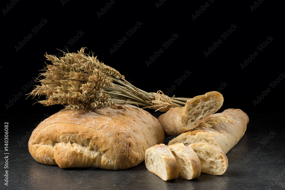 Baguette and ciabatta, bread slices on dark wooden table. Wheat and fresh mixed breads isolated on black background. Food, bakery concept