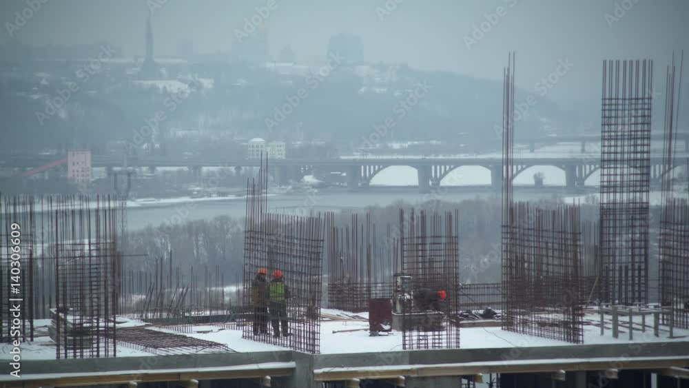 construction team at building with boss discussing work. People working outdoors in winter season built new apartment house. Men wearing in orange coveralls and hard hat.Urban view on the city with construction team at building with boss discussing work. People working outdoors in winter season built new apartment house. Men wearing in orange coveralls and hard hat.Urban view on the city with