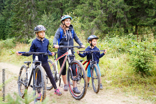 Young girl with her mother and small brother enjoying cycling in forest. Family riding bike concept background