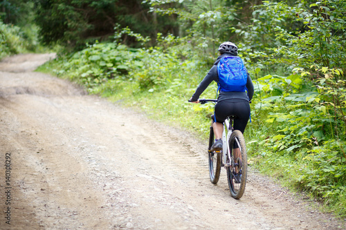 Young woman with backpack riding bicycle on mountain road in the forest