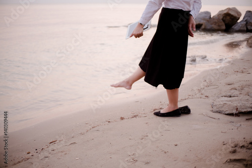 Blurred Background young business woman relaxing working Using tablet and Toe Foot touches the sea on the beach At the time of sunset . happy at work Concept .
