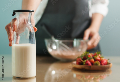 Woman hand holding  milk glass bottle with strawberries in wooden plate.