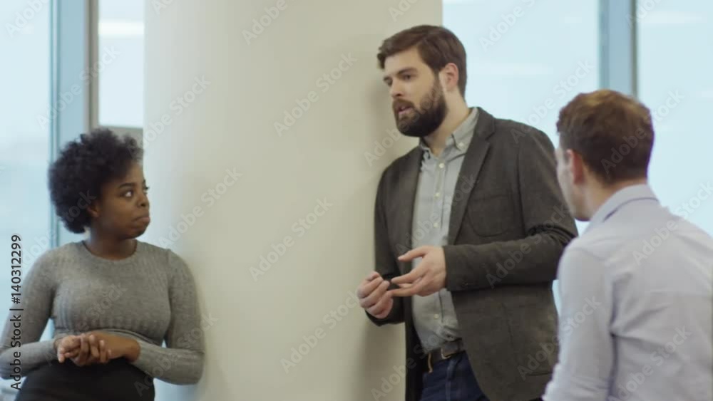 Slowmo of young bearded businessman and African woman leaning on column in office and talking to coworker at informal meeting Slowmo of young bearded businessman and African woman leaning on column in office and talking to coworker at informal meeting