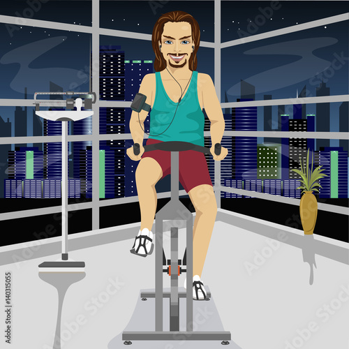 young man with smartphone armband on an exercise bike in gym in evening