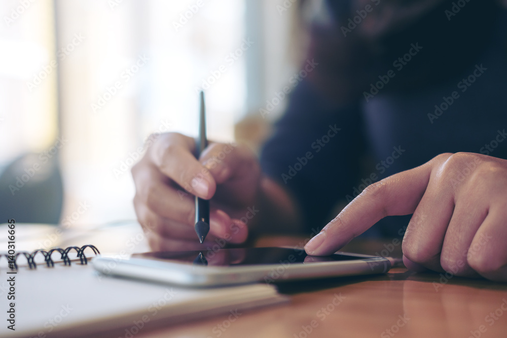 A woman's hands writing on notebook and using smartphone on wooden table in modern cafe A woman's hands writing on notebook and using smartphone on wooden table in modern cafe