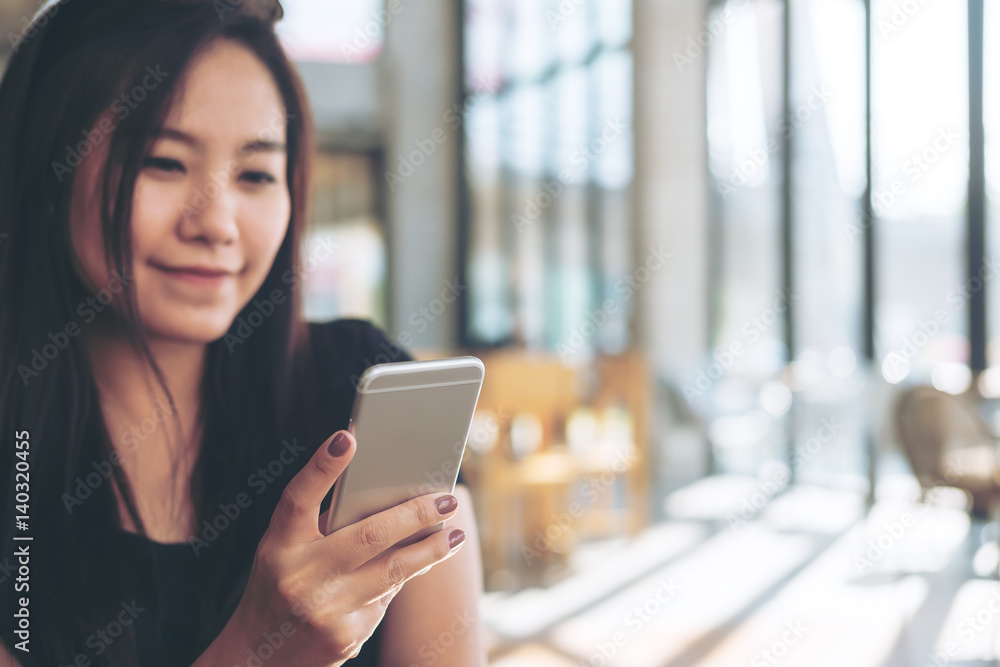 Beautiful Asian womanl with smiley face holding , using and looking at smart phone in modern cafe Beautiful Asian womanl with smiley face holding , using and looking at smart phone in modern cafe
