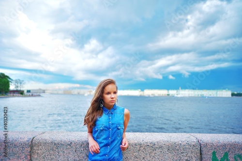 Portrait of pensive beautiful woman in a blue denim shirt  standing on the embankment in summer Sunny day.