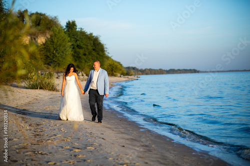 Portrait of Couple of lovers newlyweds on the seafront. Brunette bride in wedding dress with a beautiful hairstyle  veil and makeup and her husband