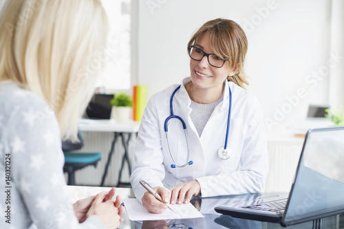 Doctor and her patient. Shot of a middle aged smiling female doctor sitting in front of laptop and meeting with her patient.