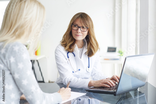 Doctor and her patient. Shot of a middle aged smiling female doctor sitting in front of laptop and meeting with her patient. photo