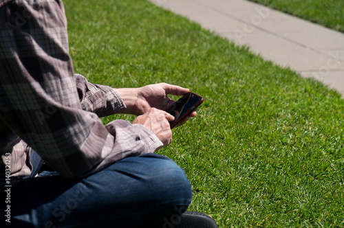 Schilderij op canvas Man sitting on grass using phone
