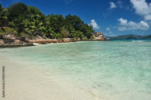 Granite stones on tropical white-sand beach next to turquoise water