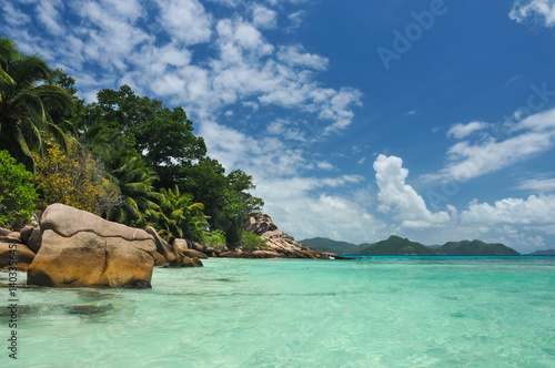 Granite stones on tropical white-sand beach next to turquoise water