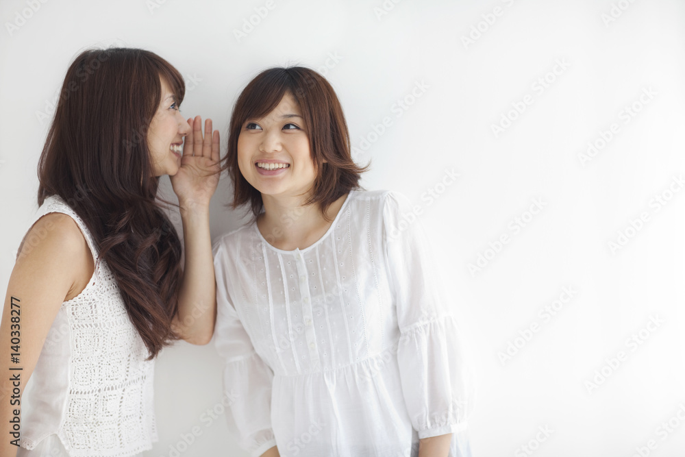 Young woman whispering friend's ear, white background, copy space Young woman whispering friend's ear, white background, copy space