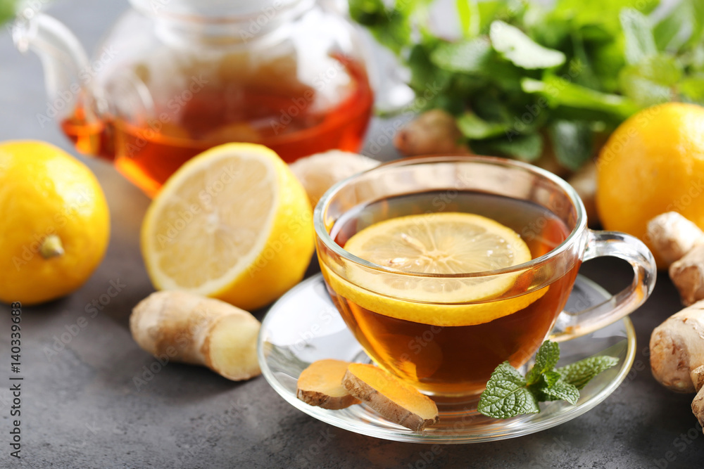 Cup of tea with ginger root and lemon on grey wooden table