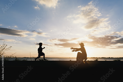 a silhouette of a happy boy child running into the arms of his loving mother for a hug  in the sunset   panoramic banner background