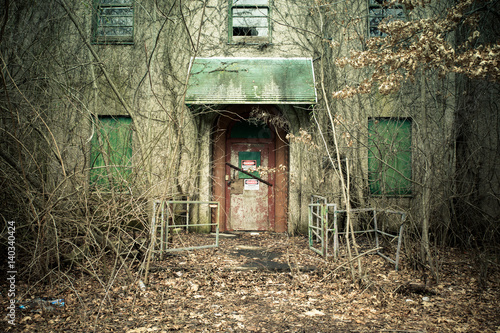 View of exterior of abandoned psychiatric hospital with asbestos warning on door