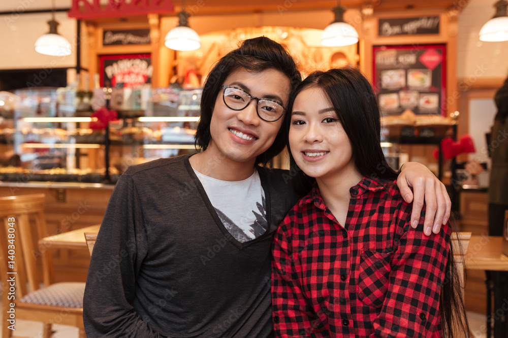 Cheerful asian young loving couple sitting in cafe indoors.