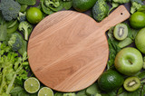 Variety of green fruits and vegetables with empty wooden cutting board. Top view, copy space.