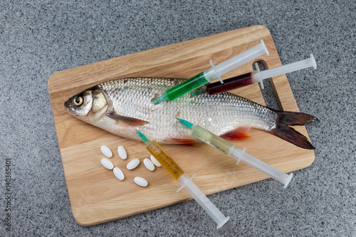 Raw fish, not cooked. White fish on a cutting Board riddled with syringes with different drugs.