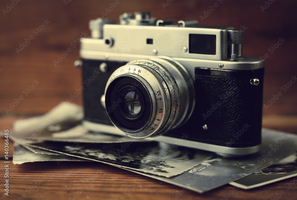Vintage photo camera with antique pictures on wooden background.