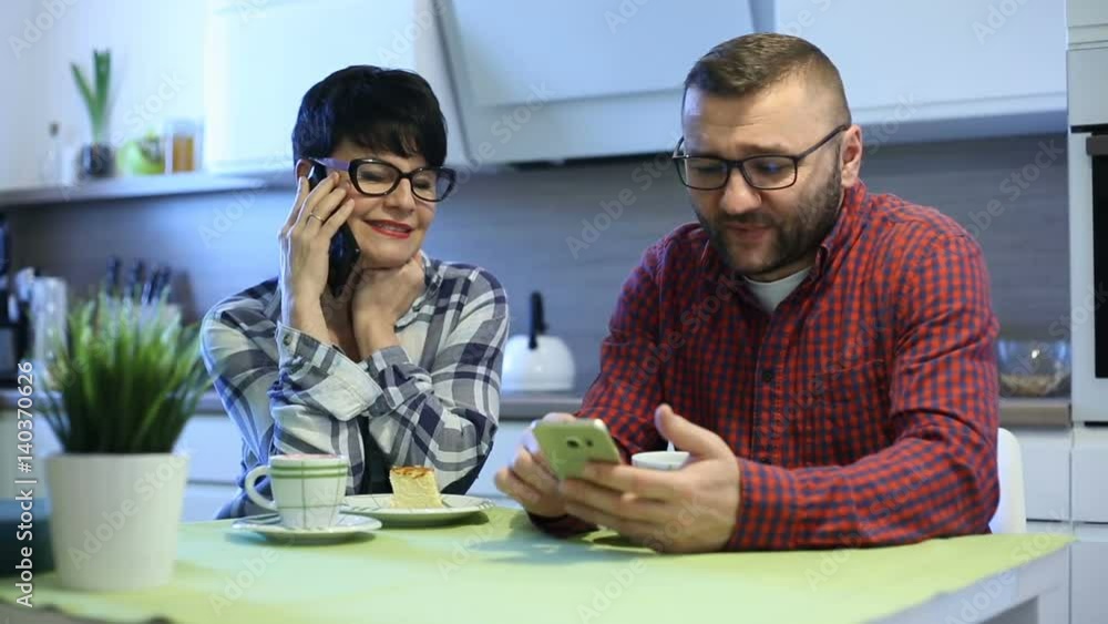 Woman chatting on cellphone while her husband is using smartphone in the kitchen
Woman chatting on cellphone while her husband is using smartphone in the kitchen