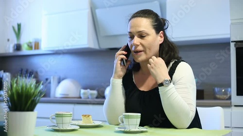 Woman looks angry while sitting in the kitchen and talking on cellphone

