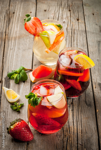 Traditional summer drink sangria - red, pink and white. With champagne, pink and red wine, strawberries, oranges, lemon, green apple and grapefruit. On a wooden rustic table, copy space 