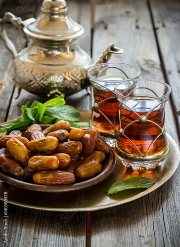 Tea with mint in arab style and dates on wooden table.