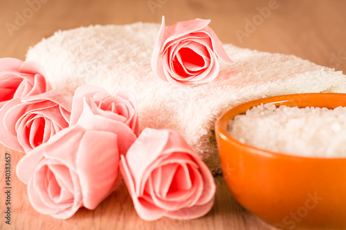 Мыло в виде цветов, морская соль в чаше и полотенце на деревянном фоне