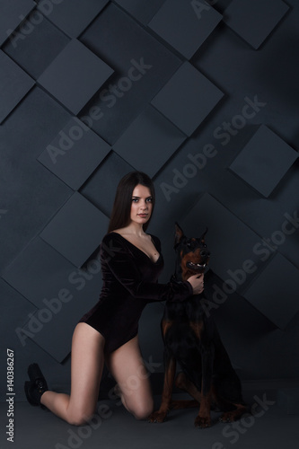 Young sexy brunette in black bodysuit with angry doberman dog. Cube background