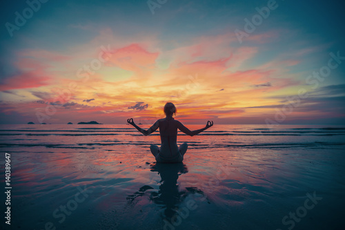 Woman yoga silhouette on the beach at amazing sunset.