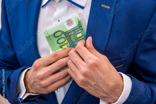 Businessman putting 100 euro bills in his pocket.