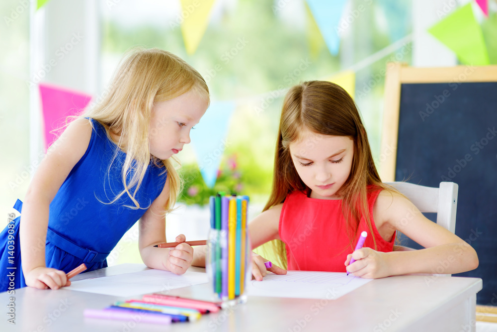 Two cute little sisters drawing with colorful pencils at a daycare. Creative kids painting together. Two cute little sisters drawing with colorful pencils at a daycare. Creative kids painting together.