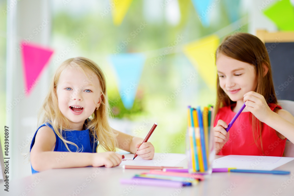 Two cute little sisters drawing with colorful pencils at a daycare. Creative kids painting together. Two cute little sisters drawing with colorful pencils at a daycare. Creative kids painting together.