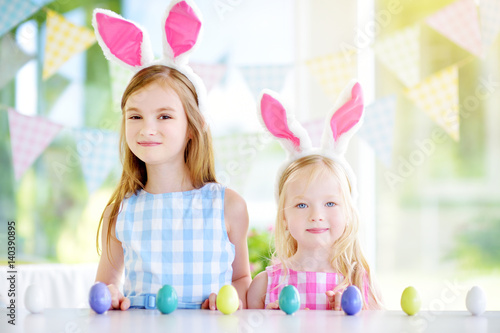 Two cute little sisters wearing bunny ears playing egg hunt on Easter