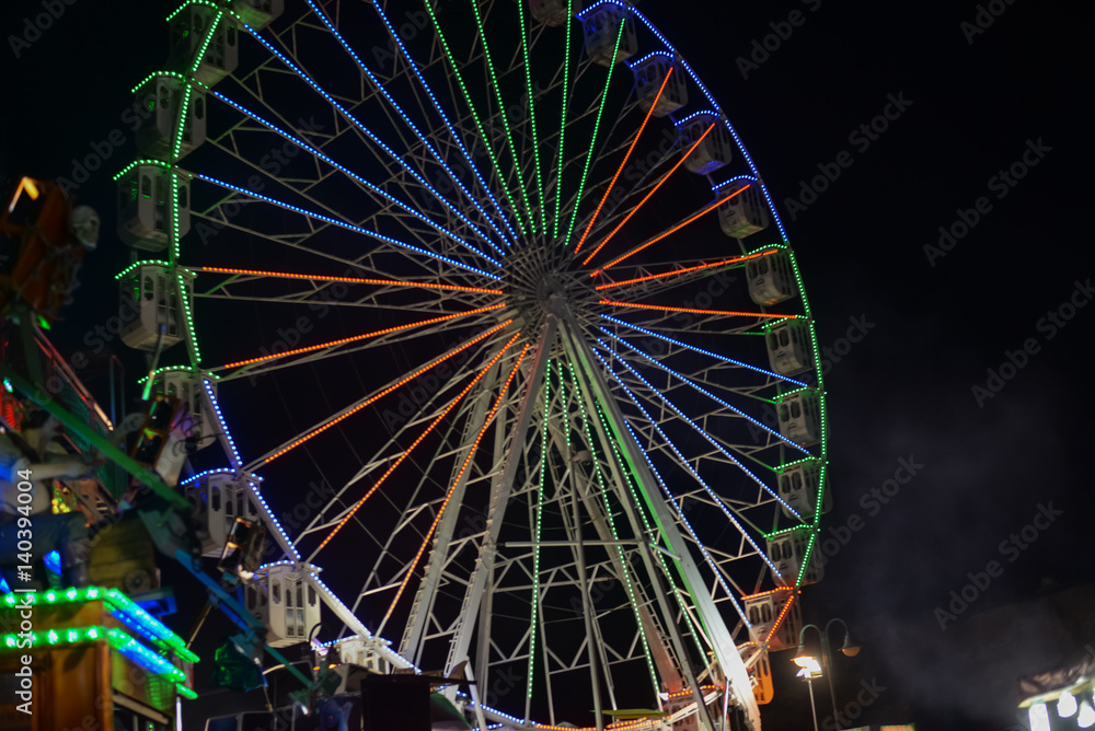 Colorful blurry lights of amusement park ferris wheel and rollercoaster on the night background