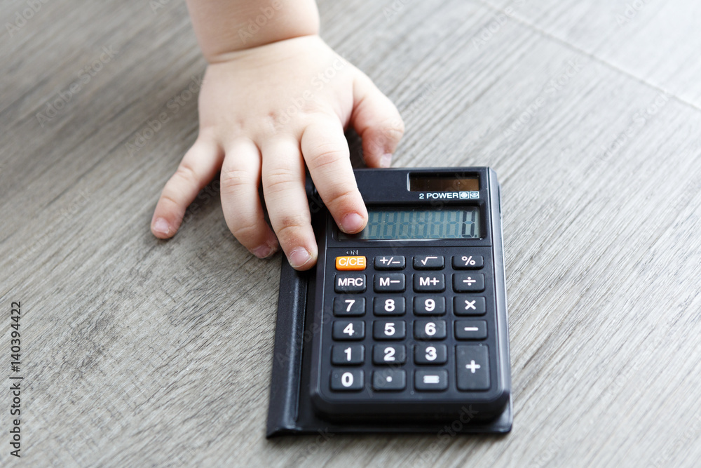 black calculator with child hand on wooden floor black calculator with child hand on wooden floor