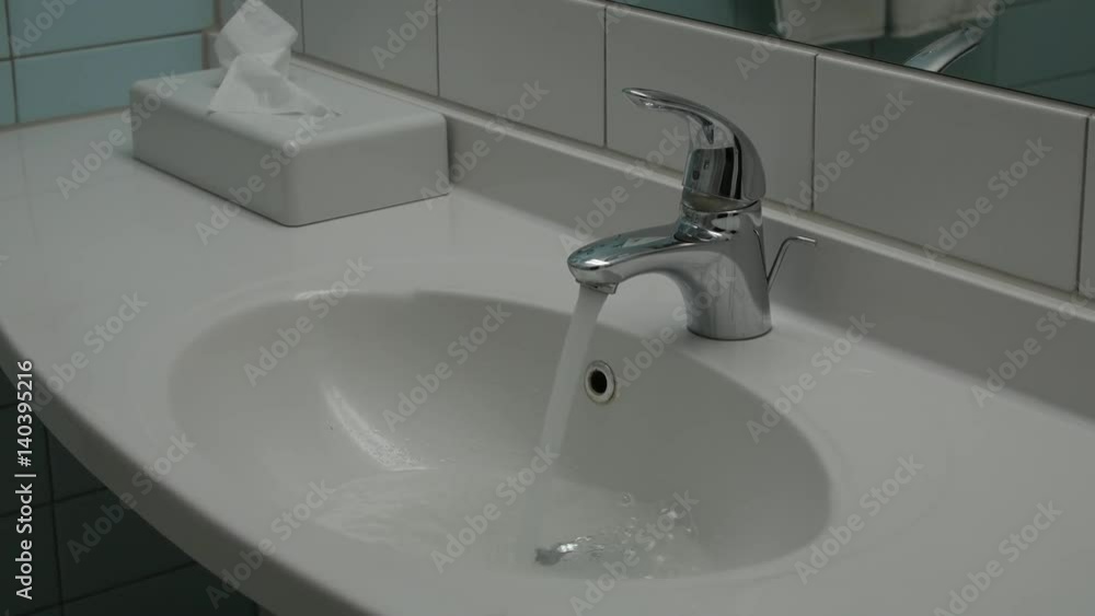 Water running continuously from water tap. Large white bathroom sink Water running continuously from water tap. Large white bathroom sink