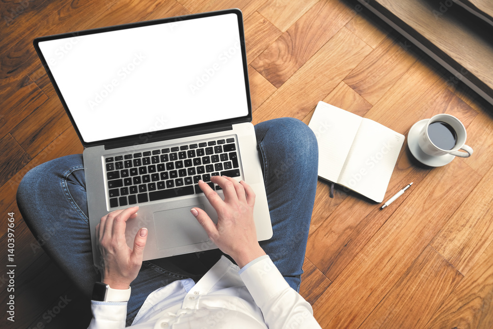 Fototapeta premium Top view of young woman sitting on the wooden floor with laptop and coffee