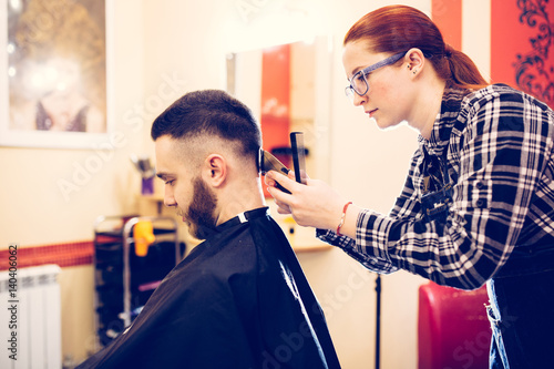 female hairdresser is cutting hair of bearded man client
