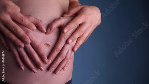 Wallpaper Mural Couple making heart shape on the pregnant naked belly with their hands, closeup on dark navy blue. Concept of pregnancy, expecting a baby, love, parenthood. 4K ProRes HQ codec Torontodigital.ca