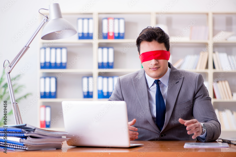 Blindfold businessman sitting at desk in office Blindfold businessman sitting at desk in office