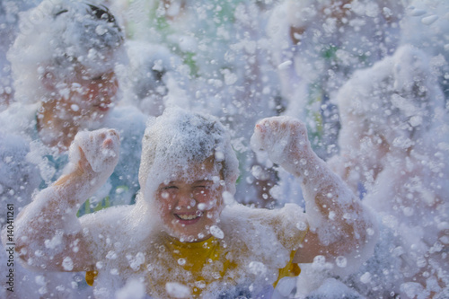 Foam Party on the beach. Cute little boy having fun and dancing.