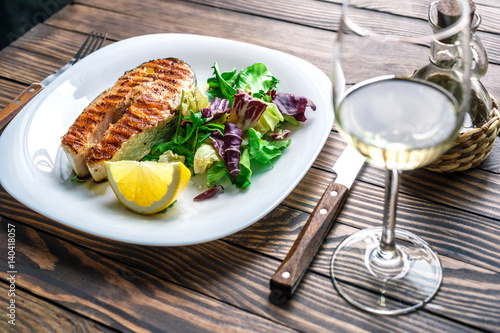 Lovely fish steak with salad, lemon and white wine on a wooden table
