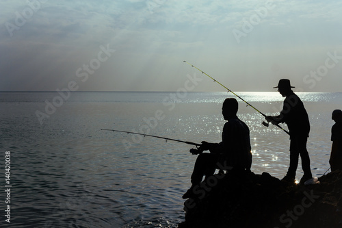 The fishermen at the ocean. The silhouettes of people fishing at the shore in the ocean. Horizontal outdoors shot.