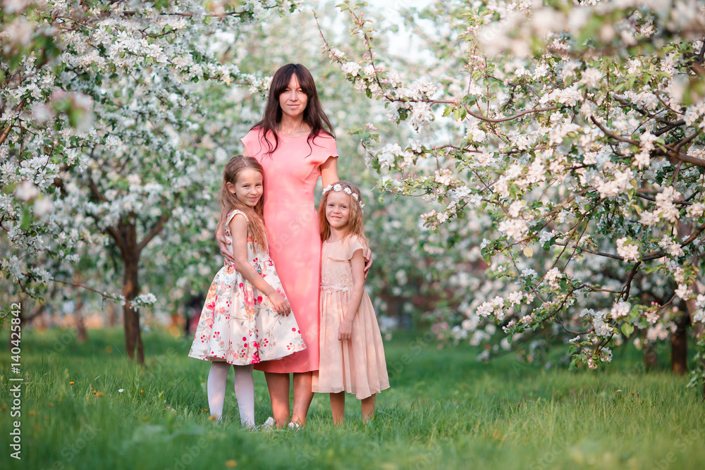 Adorable little girls with young mother in blooming cherry garden on beautiful spring day Adorable little girls with young mother in blooming cherry garden on beautiful spring day