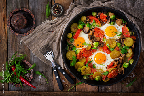 Breakfast for two. Fried eggs with vegetables - shakshuka in a frying pan on a wooden background in rustic style. Flat lay. Top view