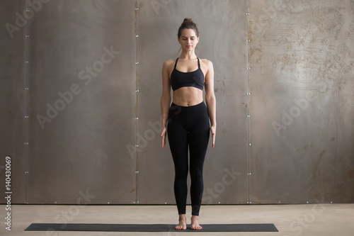 Young attractive yogi woman practicing yoga, standing in Tadasana exercise, mountain pose, working out, wearing black sportswear, cool urban style, full length, grey studio background photo